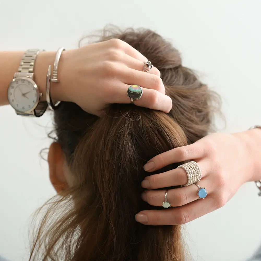 Les mains d'une jeune fille tenant ses cheveux, avec des bijoux en argent qui peuvent déteindre sur la peau