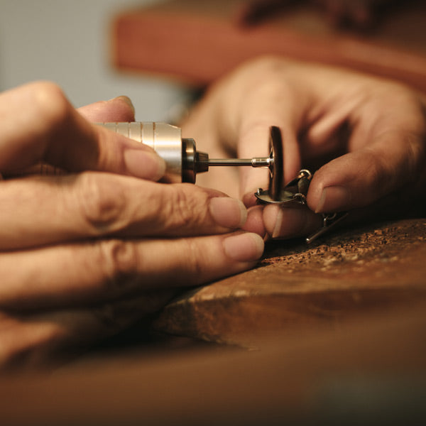 Mains d'artisan en train de travailler un bijou en atelier, prenant appui sur un établi en bois