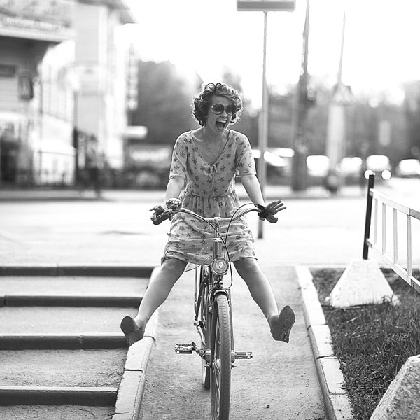 Femme à vélo représentant l'esprit libre de La Désinvolte, photo en noir et blanc, la femme lâche les pédales et profite du moment en riant